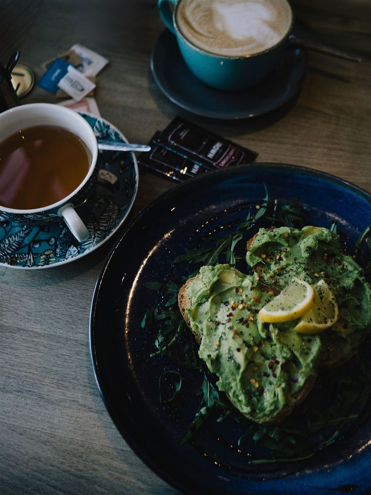 Latte, avocado toast, and a chocolate muffin spread